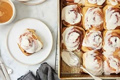 a pan filled with cinnamon rolls on top of a table next to two cups of coffee