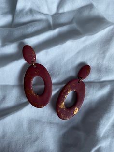 two red and gold earrings laying on top of a white sheet covered bedding,