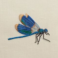 a blue dragonfly embroidered onto a white cloth