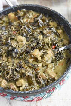 a pan filled with green food on top of a wooden table next to a spoon