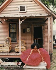 a woman in a red dress is standing on the porch of a house with furniture