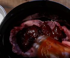 someone is pouring ketchup on meat in a skillet with other food items