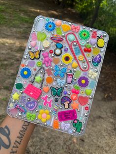 a person holding up a square case with lots of stickers and magnets on it