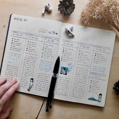 a person holding a pen and looking at a planner with ear buds on the table