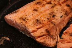 salmon being cooked in a frying pan with garlic and seasonings on it's side