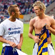 two men standing next to each other in front of a soccer field with one holding a towel