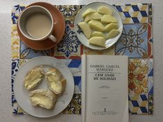 a table topped with plates of food next to a cup of coffee and a book