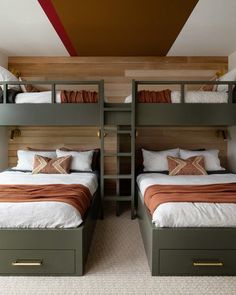 two bunk beds in a room with wooden paneling and white bedding, one has orange throw pillows on it