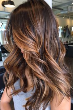 Woman with long, wavy, brunette hair featuring caramel highlights in a modern salon. Fall Balayage Brunette Honey, Warm Brown With Caramel Highlights, Brown Hair Colors For Pale Skin, Caramel Balayage Curly Hair Dark Brown, Gold Highlights On Brown Hair, Light Brown Hair With Caramel Highlights Honey, Deep Autumn Hair Color Ideas, Caramel Hair With Highlights, Lowlights On Brown Hair