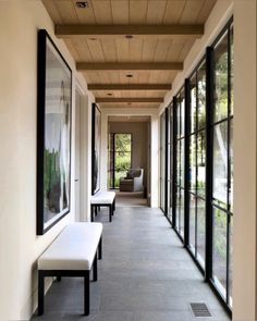 a long hallway with benches and large windows on both sides, leading to another room