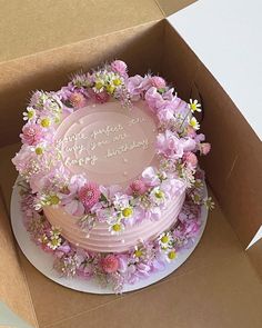 a pink cake in a box with flowers on the top and words written on it