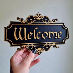 a hand holding up a black and gold welcome sign