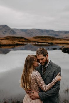 a man and woman standing next to each other in front of a lake