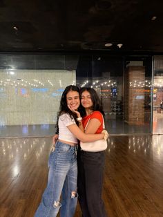 two young women hugging each other in an empty dance floor with lights on the wall behind them