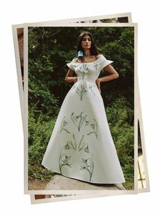 a woman in a white dress is standing on a rock with trees behind her and bushes to the side