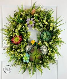 a wreath with succulents and other plants hanging on the front door frame