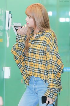 the girl is wearing a plaid shirt and holding a cell phone in her hand while standing next to a green wall