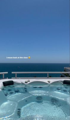 a hot tub sitting on top of a wooden deck next to the ocean in front of a blue sky