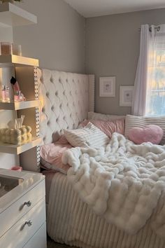 a white bed sitting next to a window in a bedroom under a blanket and pillows