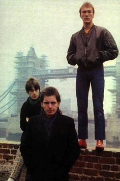 two men and a child are standing on a brick wall in front of a bridge