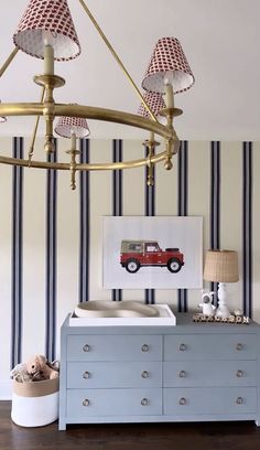 a baby's room with blue dresser and striped wallpaper, including a red car