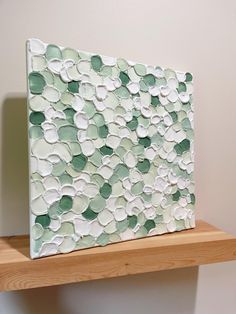 a white and green painting sitting on top of a wooden shelf