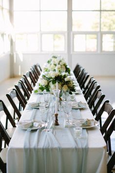 a long table with white and green flowers on it is set for a formal dinner