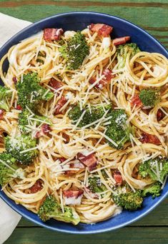 a blue bowl filled with pasta and broccoli on top of a wooden table