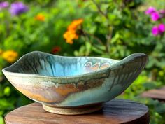 a bowl sitting on top of a wooden table in front of some plants and flowers