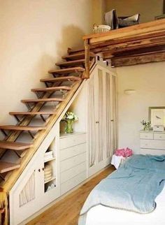 a bed sitting under a wooden staircase next to a white dresser in a room with wood floors