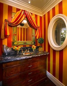 the bathroom is decorated in red and yellow striped wallpaper, along with an oval mirror