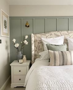 a white bed sitting in a bedroom next to a nightstand with flowers on top of it