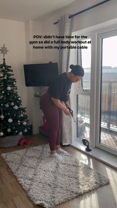 a woman standing on top of a rug in front of a window next to a christmas tree