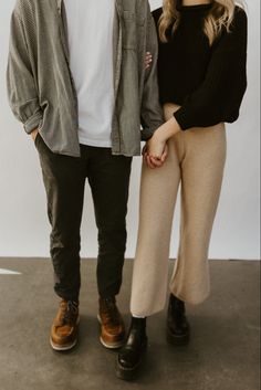 a man and woman standing next to each other in front of a white wall holding hands