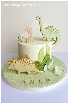 a birthday cake decorated with dinosaurs and eggs on a green platter that says 1st birthday