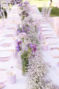 a long table with purple and white flowers on it, along with plates and cups