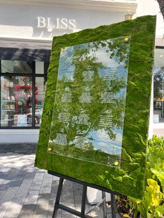 a large green sign sitting on top of a sidewalk next to a planter filled with flowers