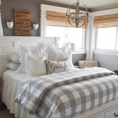 a white bed sitting under a window next to a chandelier in a bedroom