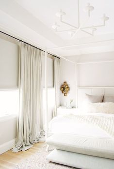 a white bed sitting in a bedroom next to a window with drapes on it