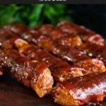 several pieces of meat sitting on top of a wooden cutting board with sauce over them