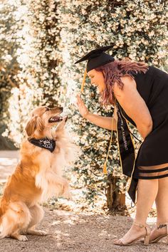 a woman kneeling down next to a brown and white dog wearing a black graduation hat