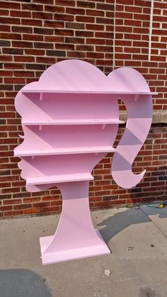 a pink shelf sitting on the side of a brick wall next to a sidewalk with a large head