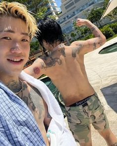 a man with tattoos on his back standing next to another man in shorts and a shirt