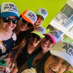 a group of women standing next to each other in front of a green building wearing hats