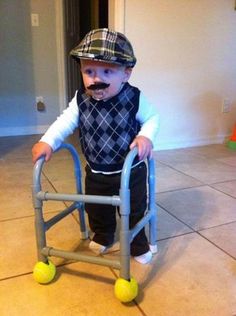 a little boy that is standing up with a walker in front of him and wearing a hat