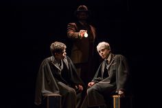 two men sitting on top of suitcases in front of a man standing behind them