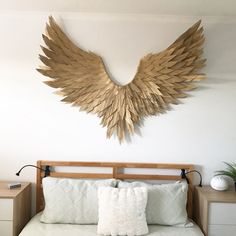 a bed with white sheets and pillows in front of a large wooden angel wings wall decoration