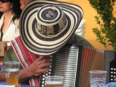 an old man wearing a hat and playing the accordion in front of people sitting at a table