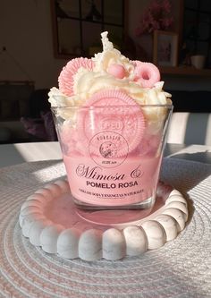 a pink and white dessert in a glass cup on top of a round tablecloth