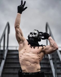 a man with no shirt on holding his hands up in the air while standing next to stairs